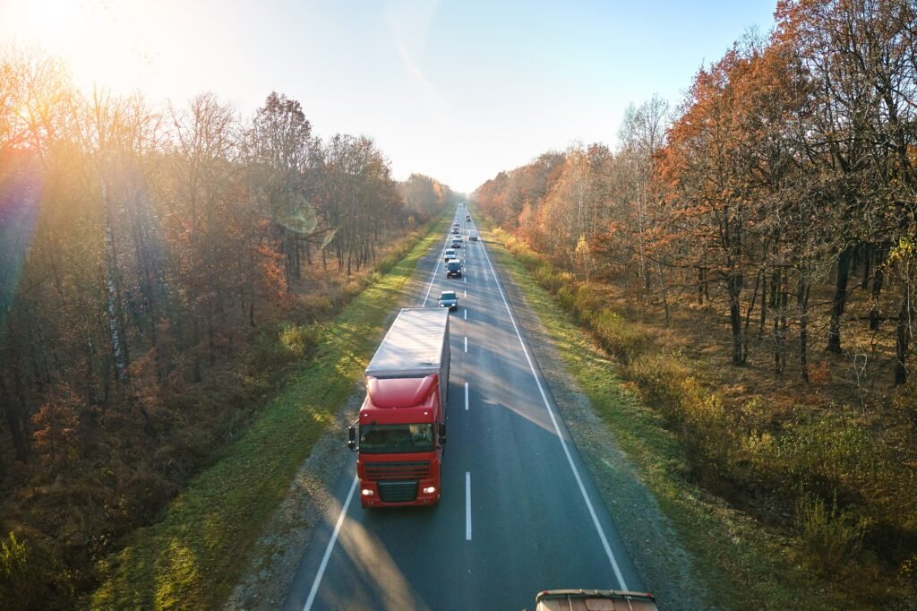 Aerial view of semi-truck with cargo trailer driving on highway hauling goods in evening. Delivery